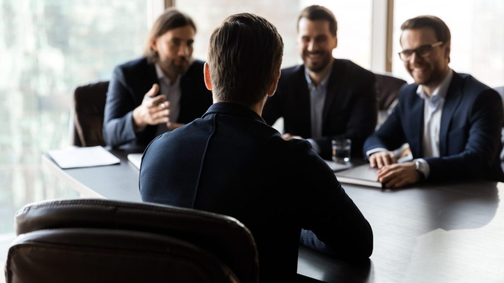 4 People in a business meeting with 3 facing the camera and 1 facing towards the others.